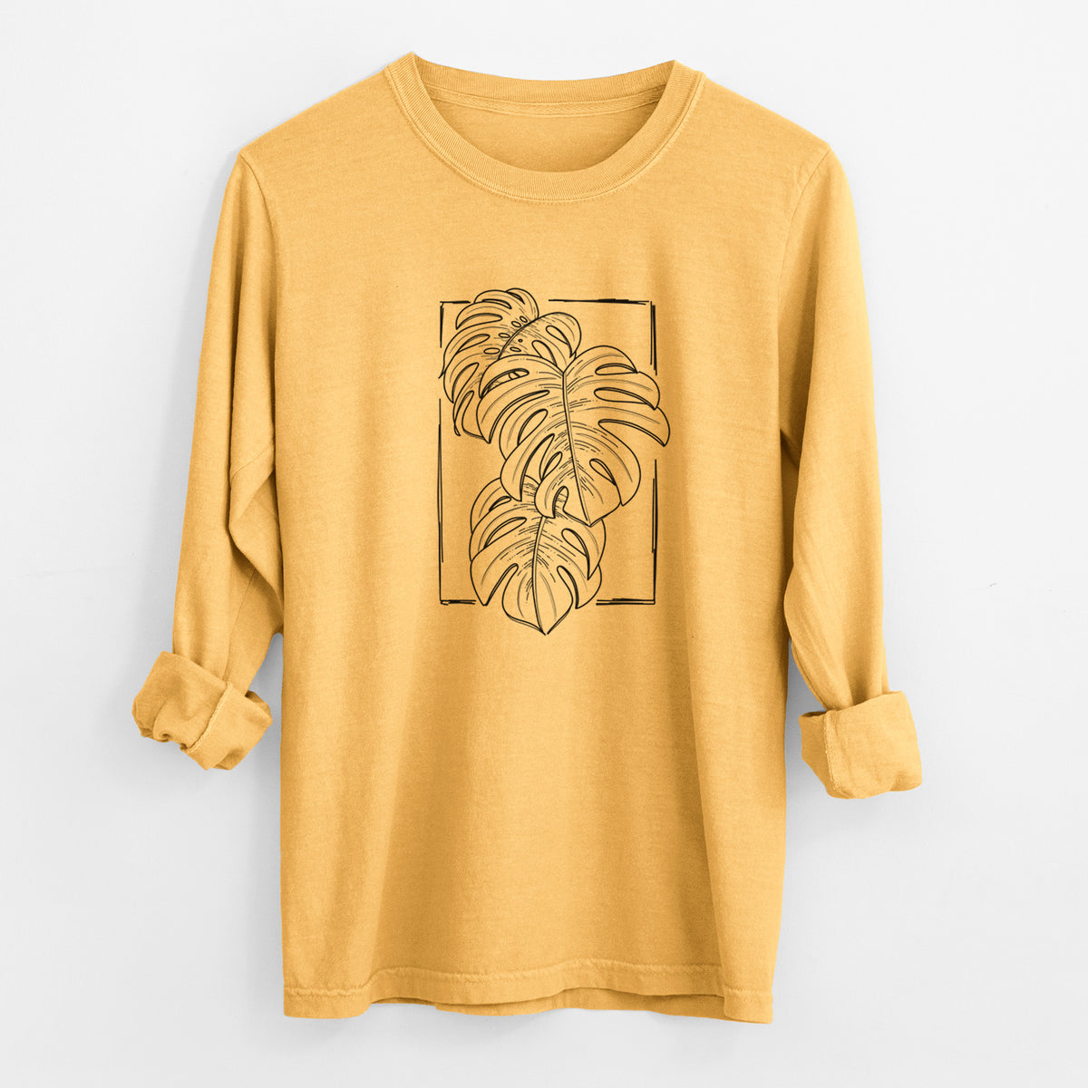 Golden wheat yellow Comfort Colors long sleeve shirt laid flat with the cuffs rolled, printed with a black ink line drawing of Monstera deliciosa leaves inside a rectangle outline.