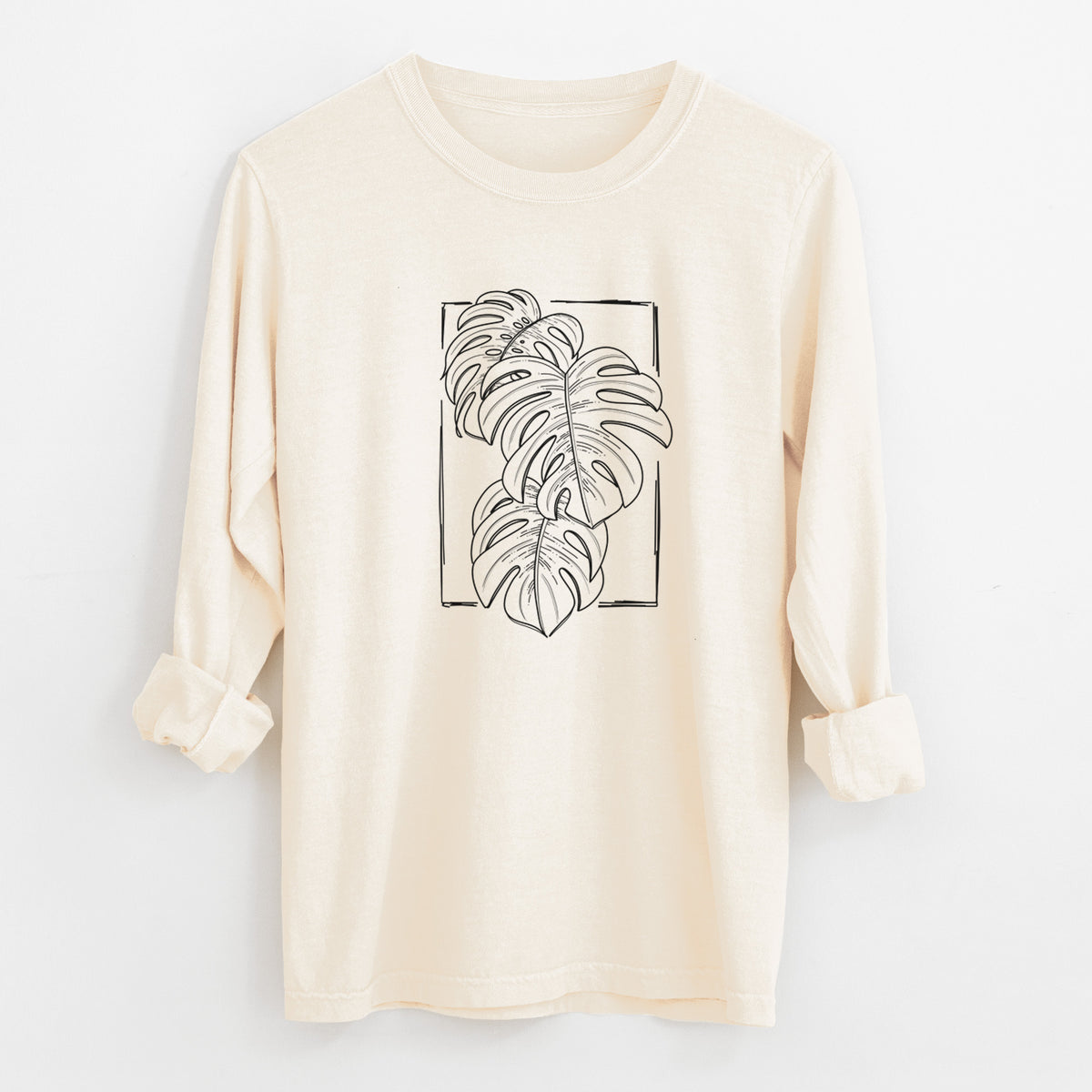 Ivory Comfort Colors long sleeve shirt laid flat with the cuffs rolled, printed with a black ink line drawing of Monstera deliciosa leaves inside a rectangle outline.