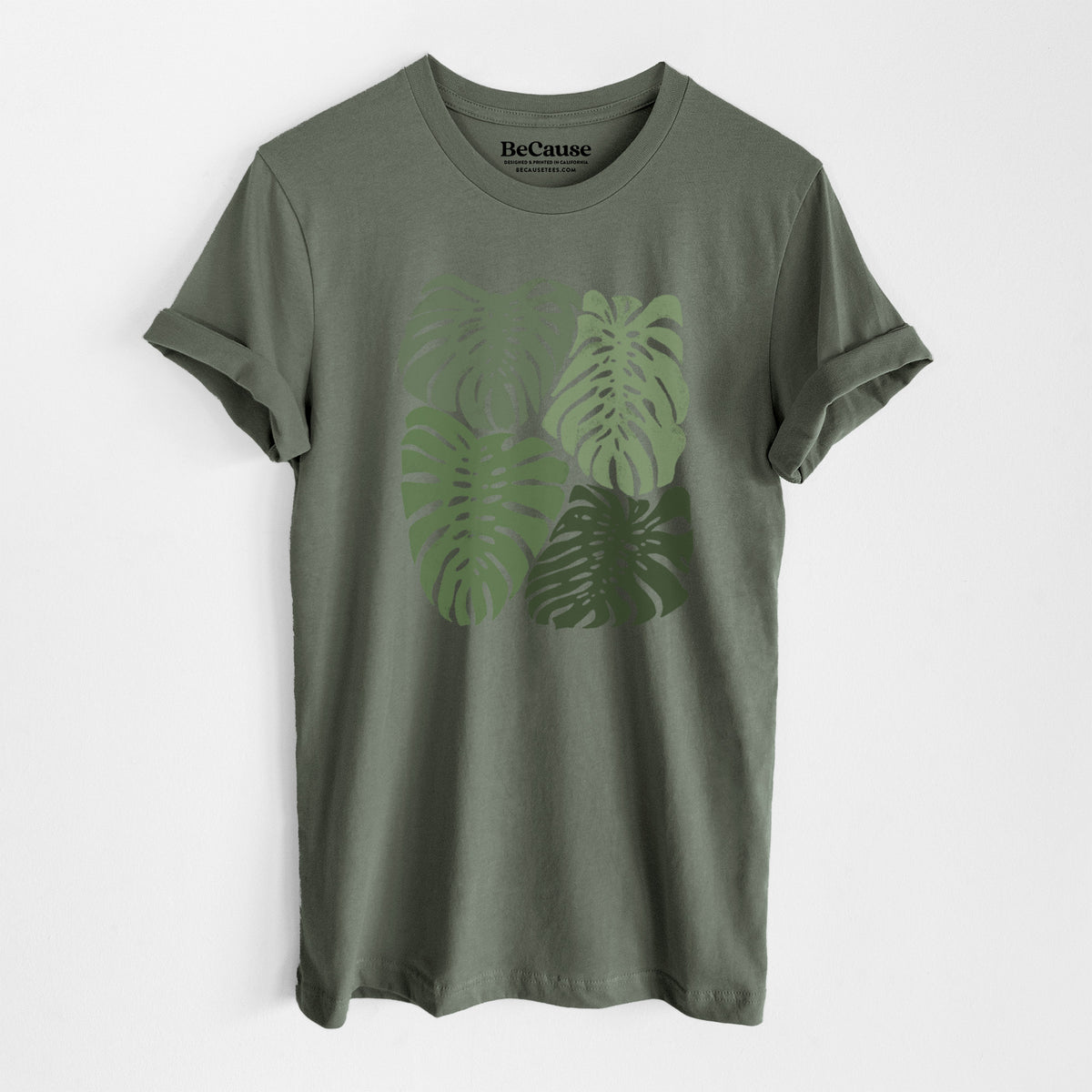 Military green lightweight cotton t-shirt laid flat, printed with a full-color illustration of large green Monstera leaves filling a square.