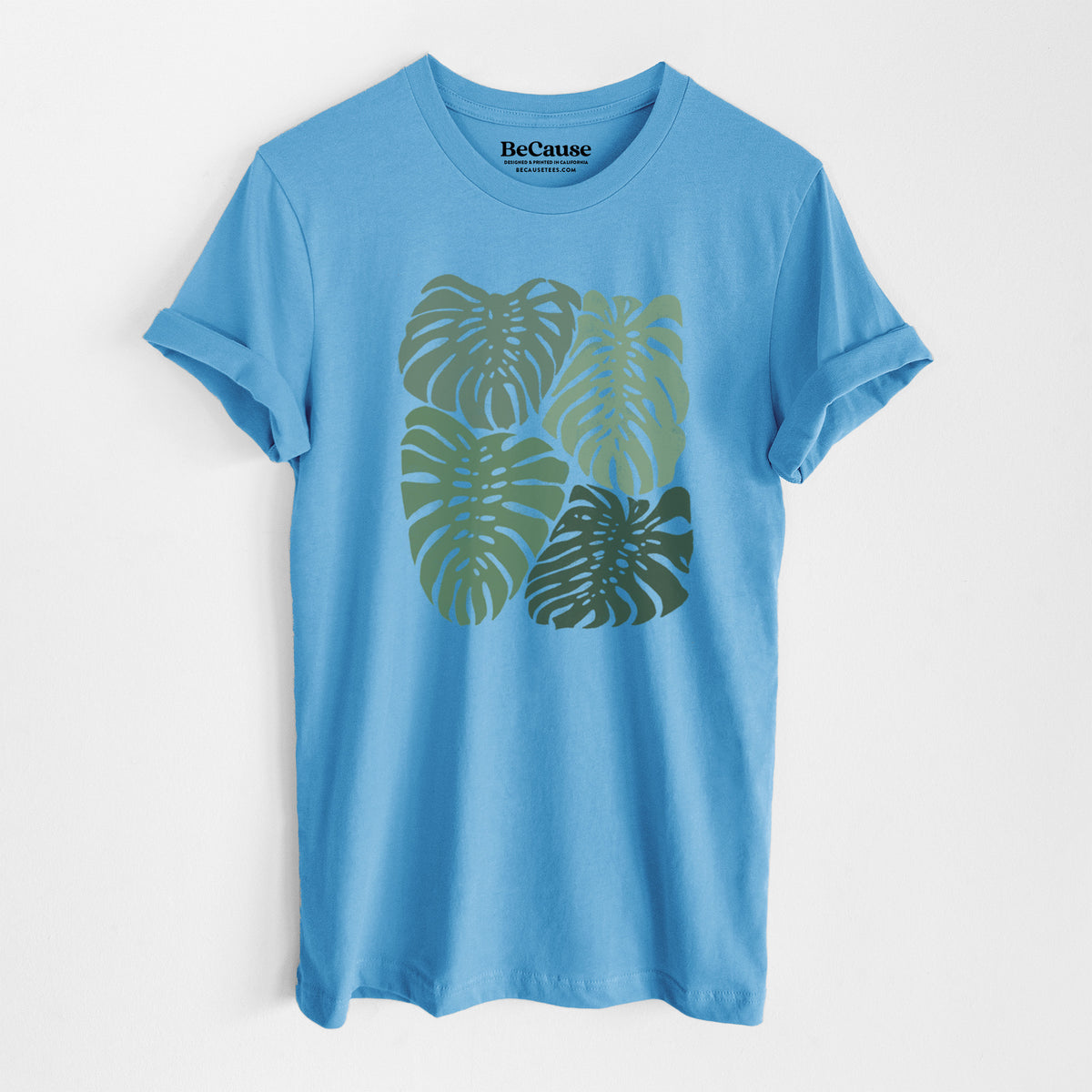 Ocean blue lightweight cotton t-shirt laid flat, printed with a full-color illustration of large green Monstera leaves filling a square.
