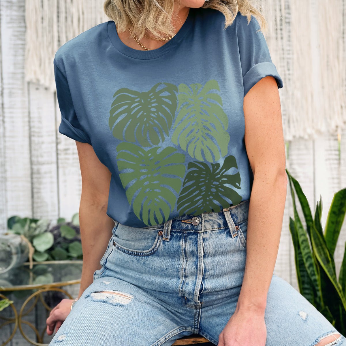 Woman wearing a steel blue lightweight cotton t-shirt printed with a full-color illustration of large green Monstera leaves filling a square.