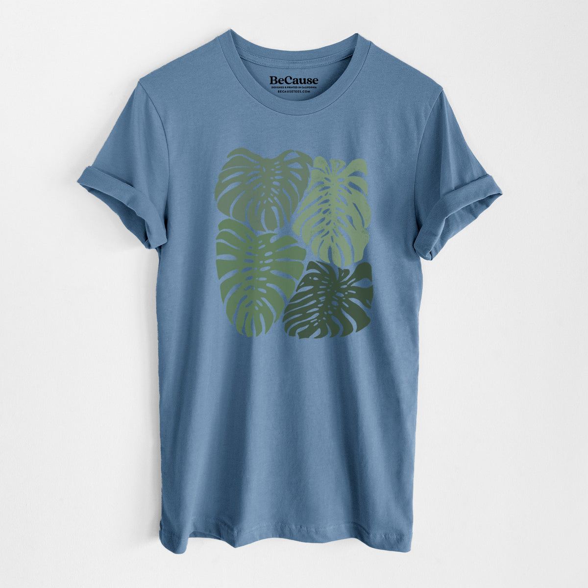 Steel blue lightweight cotton t-shirt laid flat, printed with a full-color illustration of large green Monstera leaves filling a square.