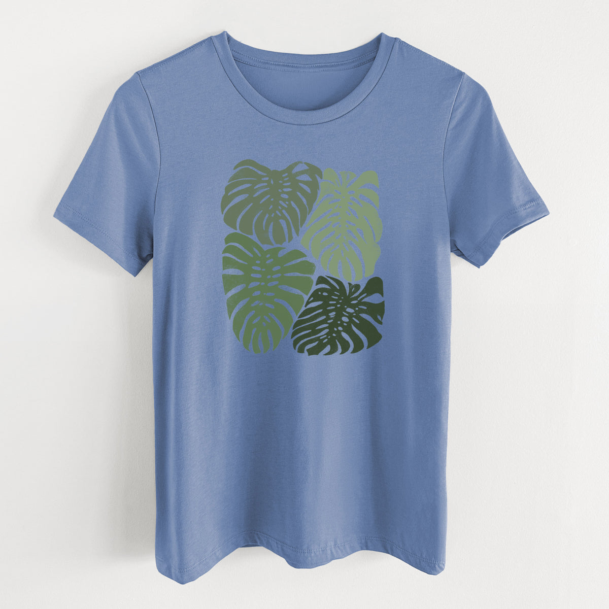Blue bell women's relaxed fit cotton t-shirt laid flat, printed with a full-color illustration of large green Monstera leaves filling a square.