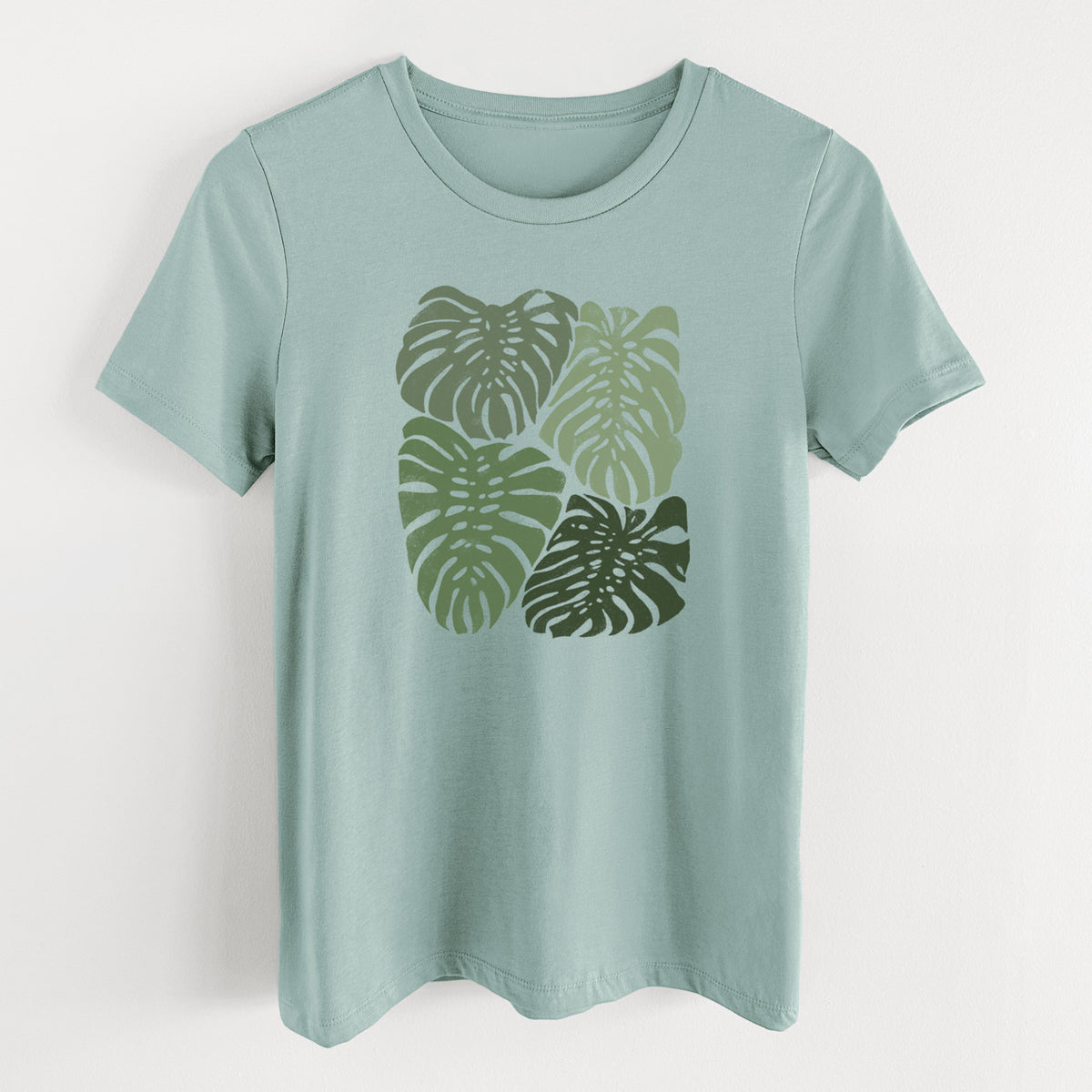 Dusty blue women's relaxed fit cotton t-shirt laid flat, printed with a full-color illustration of large green Monstera leaves filling a square.