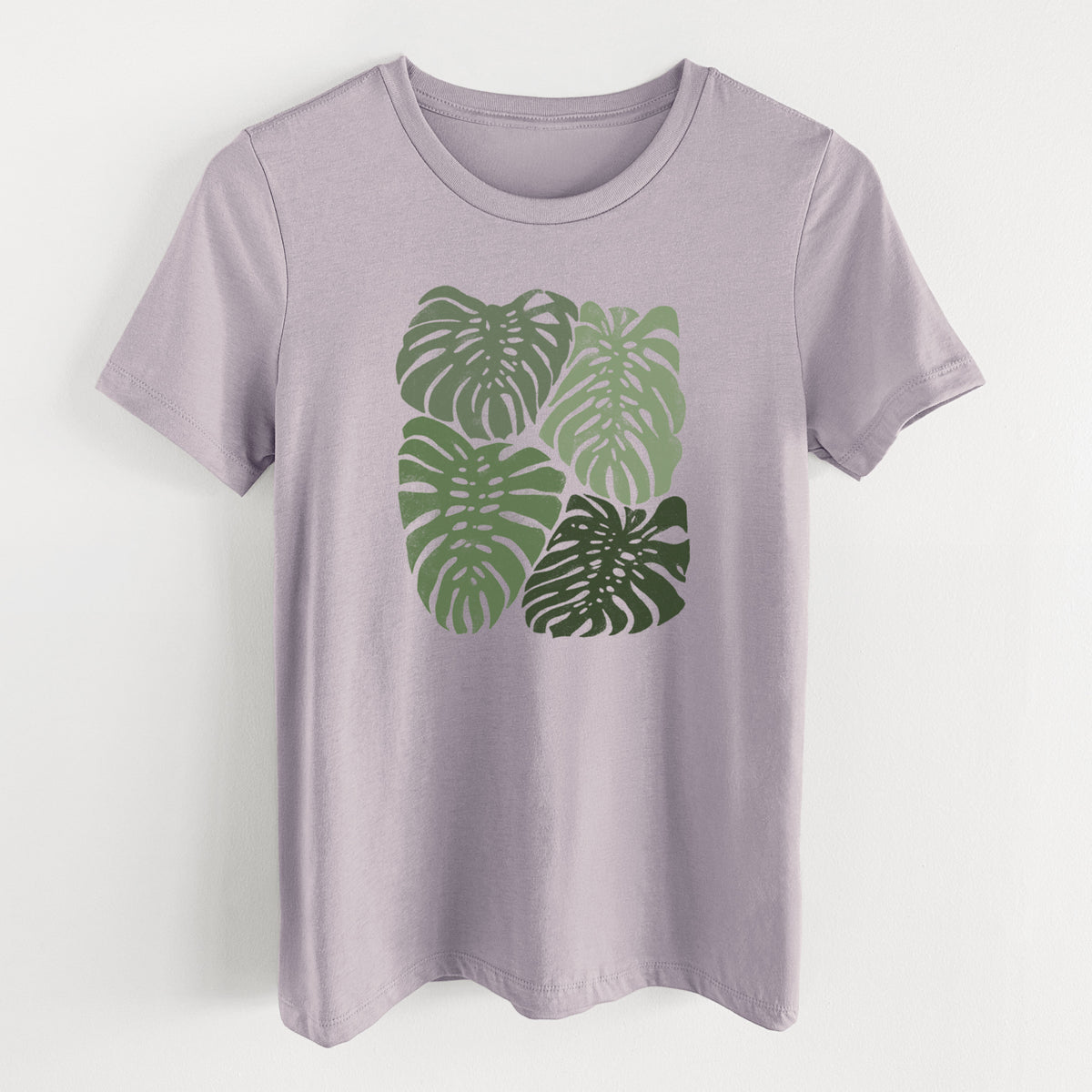 Light violet women's relaxed fit cotton t-shirt laid flat, printed with a full-color illustration of large green Monstera leaves filling a square.