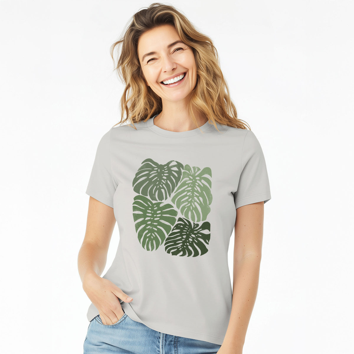 Woman wearing a lunar grey women's relaxed fit cotton t-shirt printed with a full-color illustration of large green Monstera leaves filling a square.