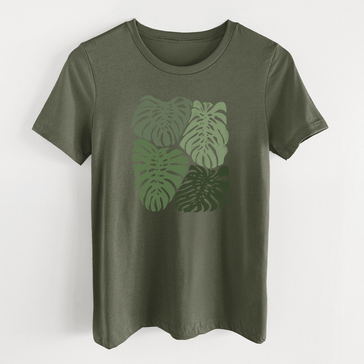 Military green women's relaxed fit cotton t-shirt laid flat, printed with a full-color illustration of large green Monstera leaves filling a square.