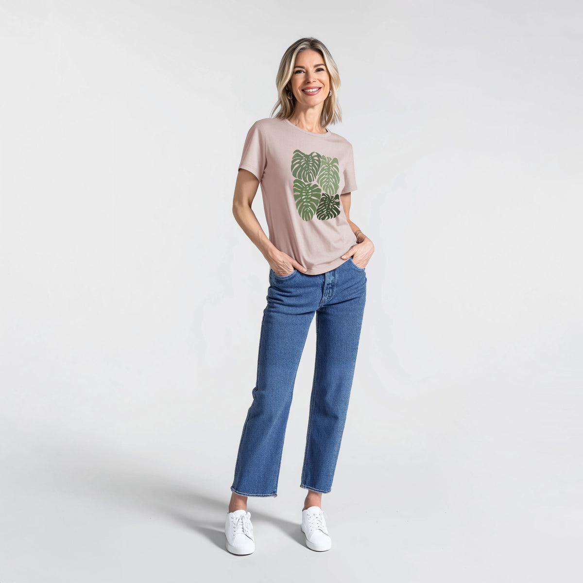 Woman wearing a pink gravel women's relaxed fit cotton t-shirt printed with a full-color illustration of large green Monstera leaves filling a square.