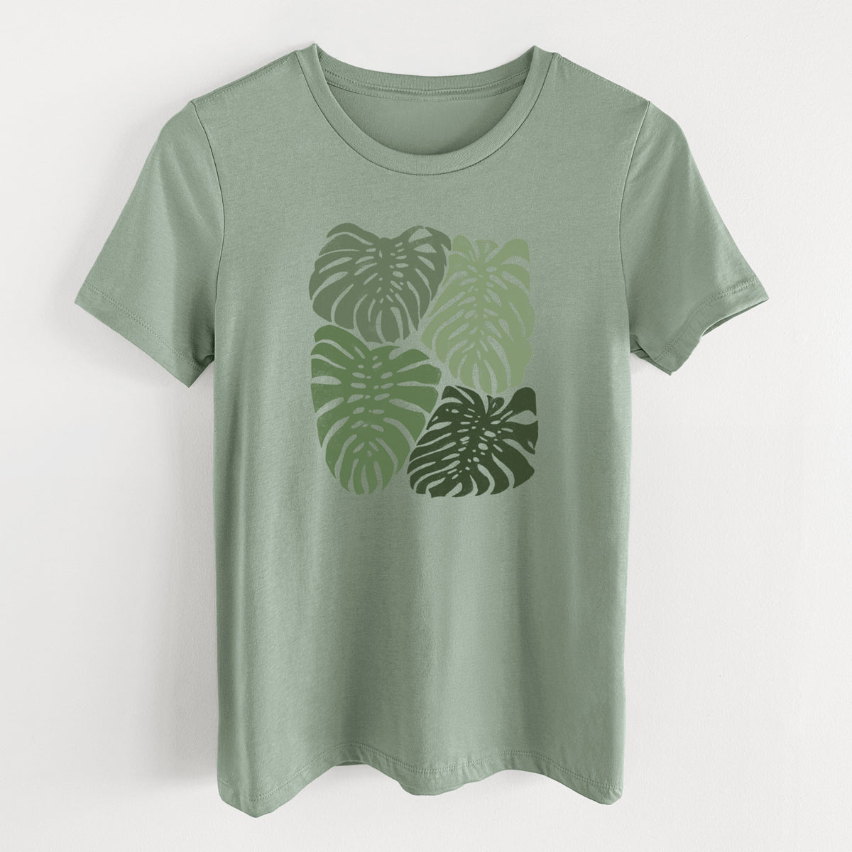 Sage green women's relaxed fit cotton t-shirt laid flat, printed with a full-color illustration of large green Monstera leaves filling a square.
