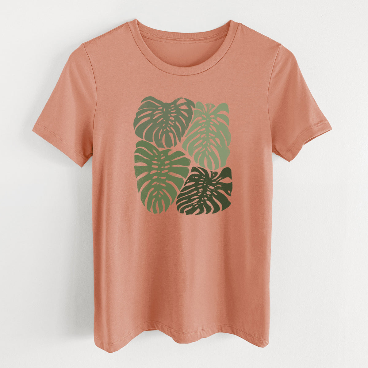 Terracotta orange women's relaxed fit cotton t-shirt laid flat, printed with a full-color illustration of large green Monstera leaves filling a square.