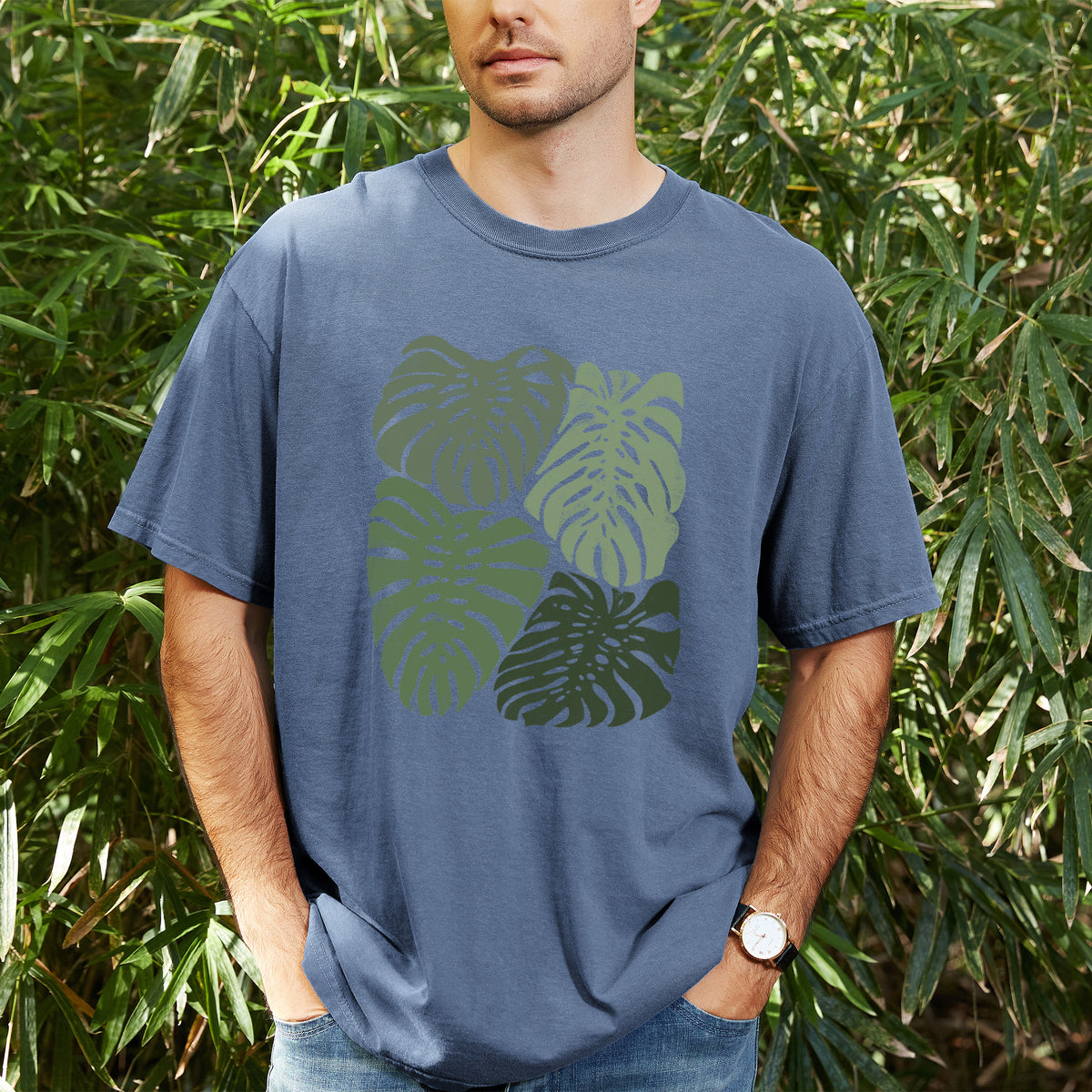 Man wearing a Comfort Colors t-shirt printed with a full-color illustration of large green Monstera leaves filling a square, outdoors.