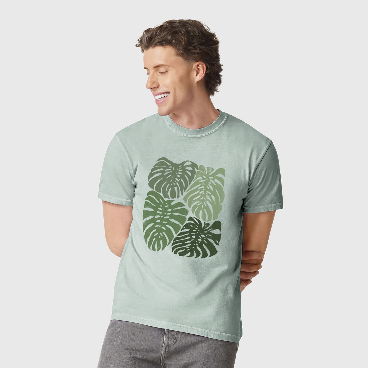 Man wearing a Comfort Colors t-shirt printed with a full-color illustration of large green Monstera leaves filling a square.