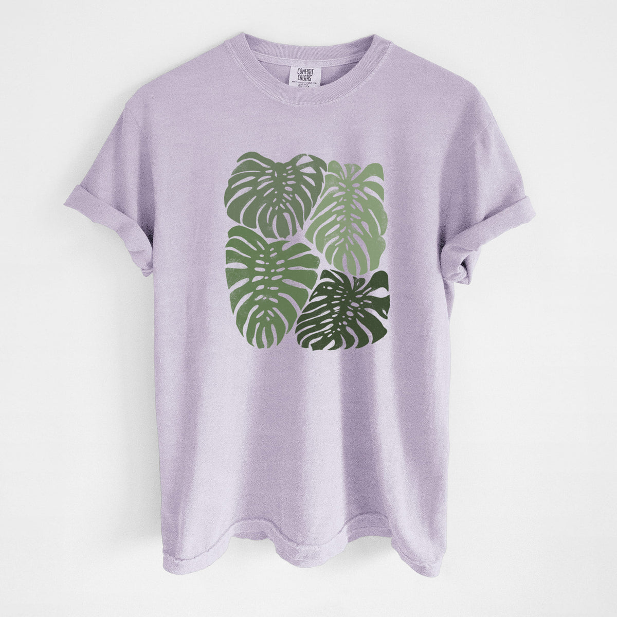 Orchid purple Comfort Colors t-shirt laid flat, printed with a full-color illustration of large green Monstera leaves filling a square.