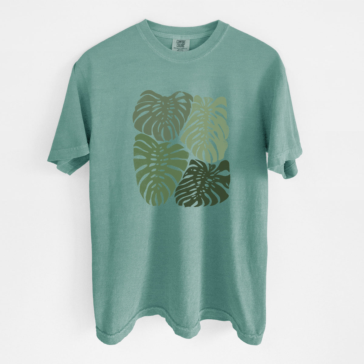 Reef green Comfort Colors t-shirt laid flat, printed with a full-color illustration of large green Monstera leaves filling a square.