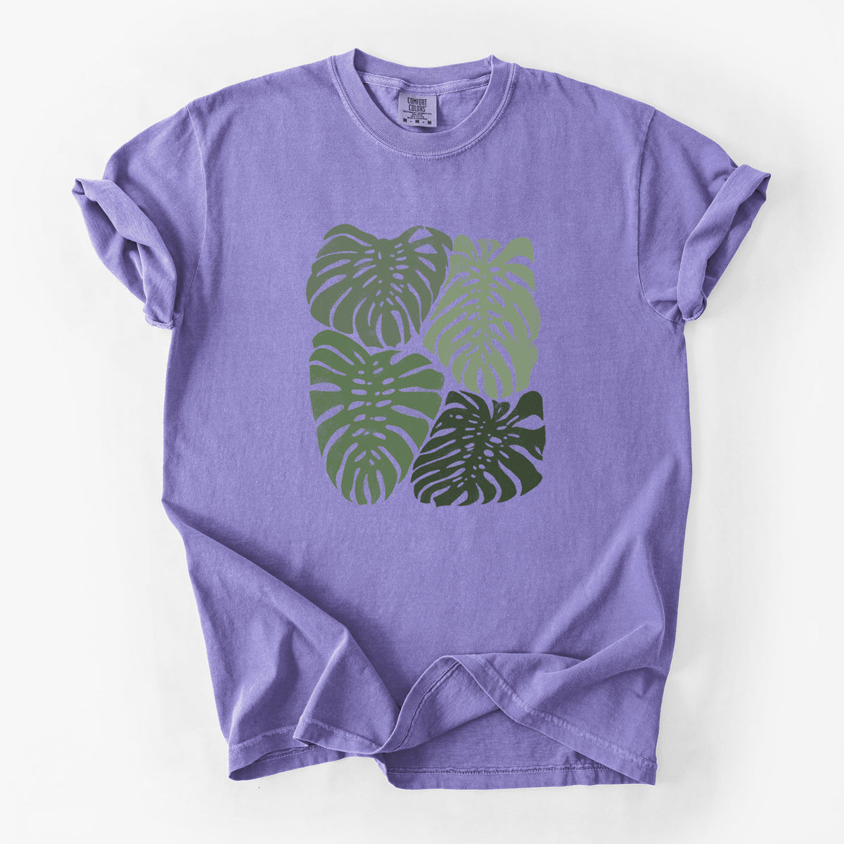 Violet purple Comfort Colors t-shirt laid flat, printed with a full-color illustration of large green Monstera leaves filling a square.