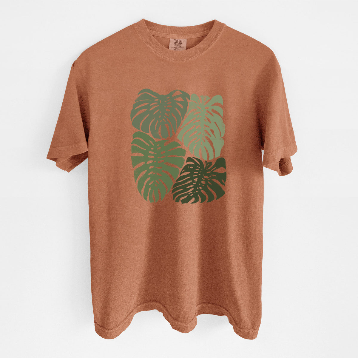 Yam burnt orange Comfort Colors t-shirt laid flat, printed with a full-color illustration of large green Monstera leaves filling a square.