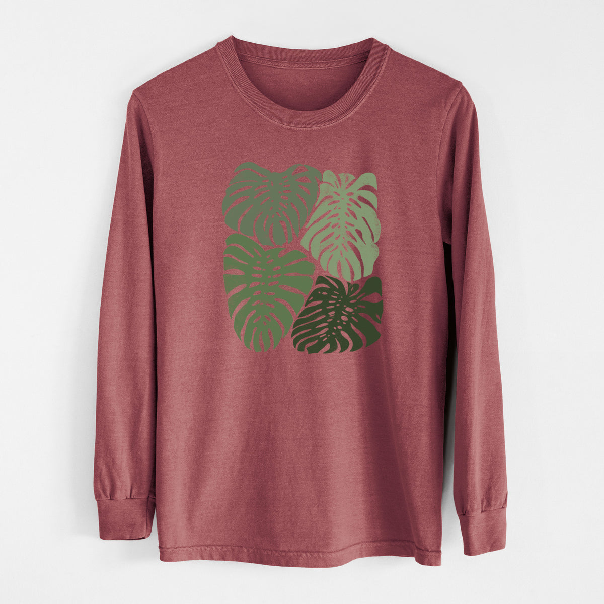 Brick red Comfort Colors long sleeve shirt laid flat, printed with a full-color illustration of large green Monstera leaves filling a square.
