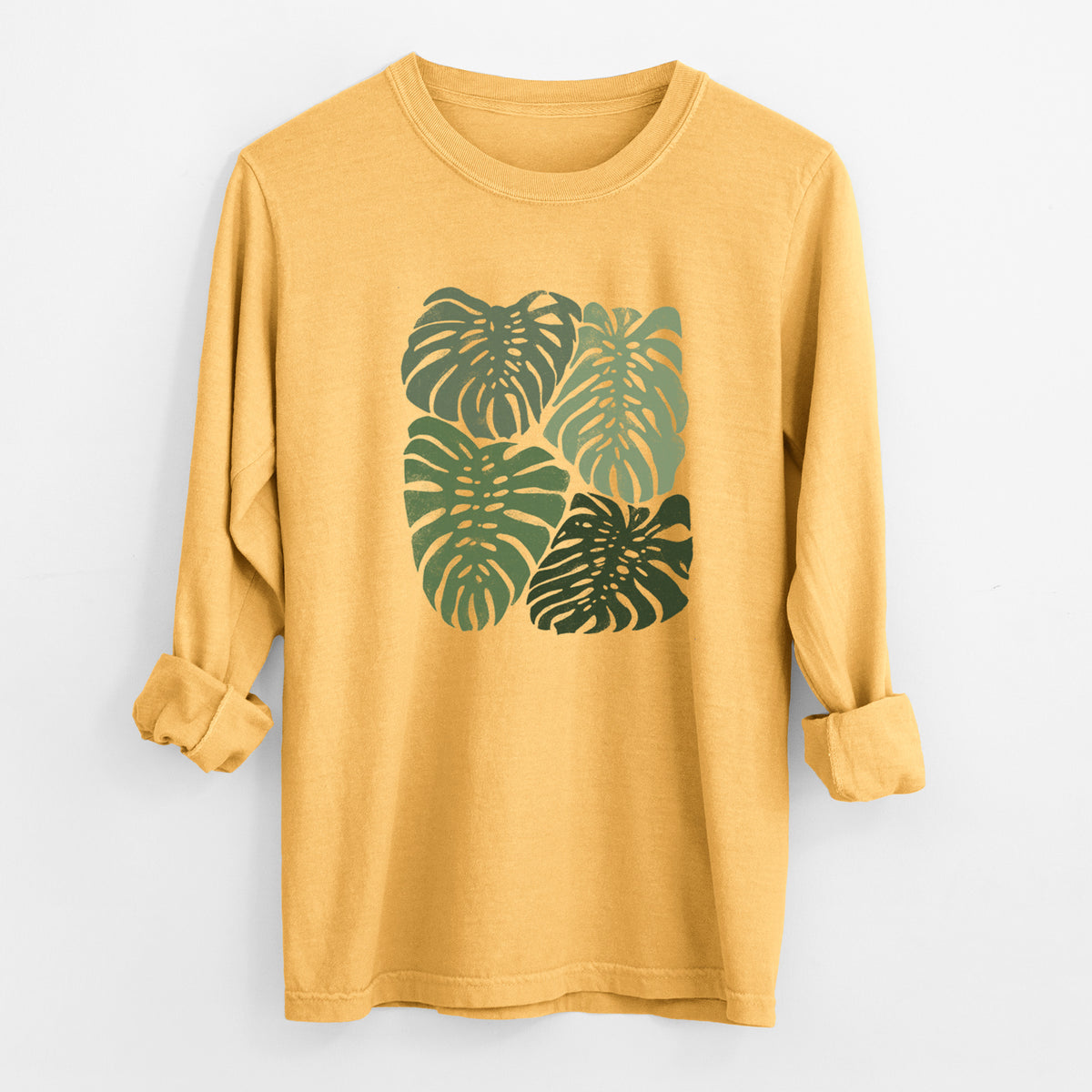 Golden wheat yellow Comfort Colors long sleeve shirt laid flat with the cuffs rolled, printed with a full-color illustration of large green Monstera leaves filling a square.
