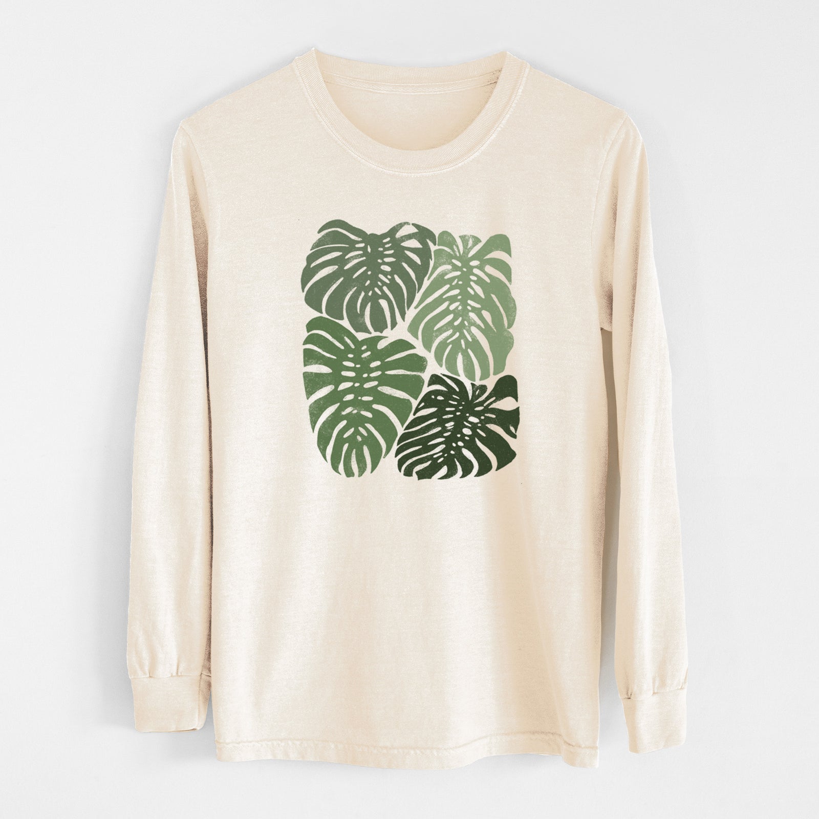 Ivory Comfort Colors long sleeve shirt laid flat, printed with a full-color illustration of large green Monstera leaves filling a square.