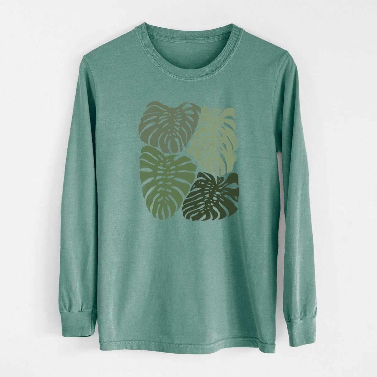 Pine green Comfort Colors long sleeve shirt laid flat, printed with a full-color illustration of large green Monstera leaves filling a square.