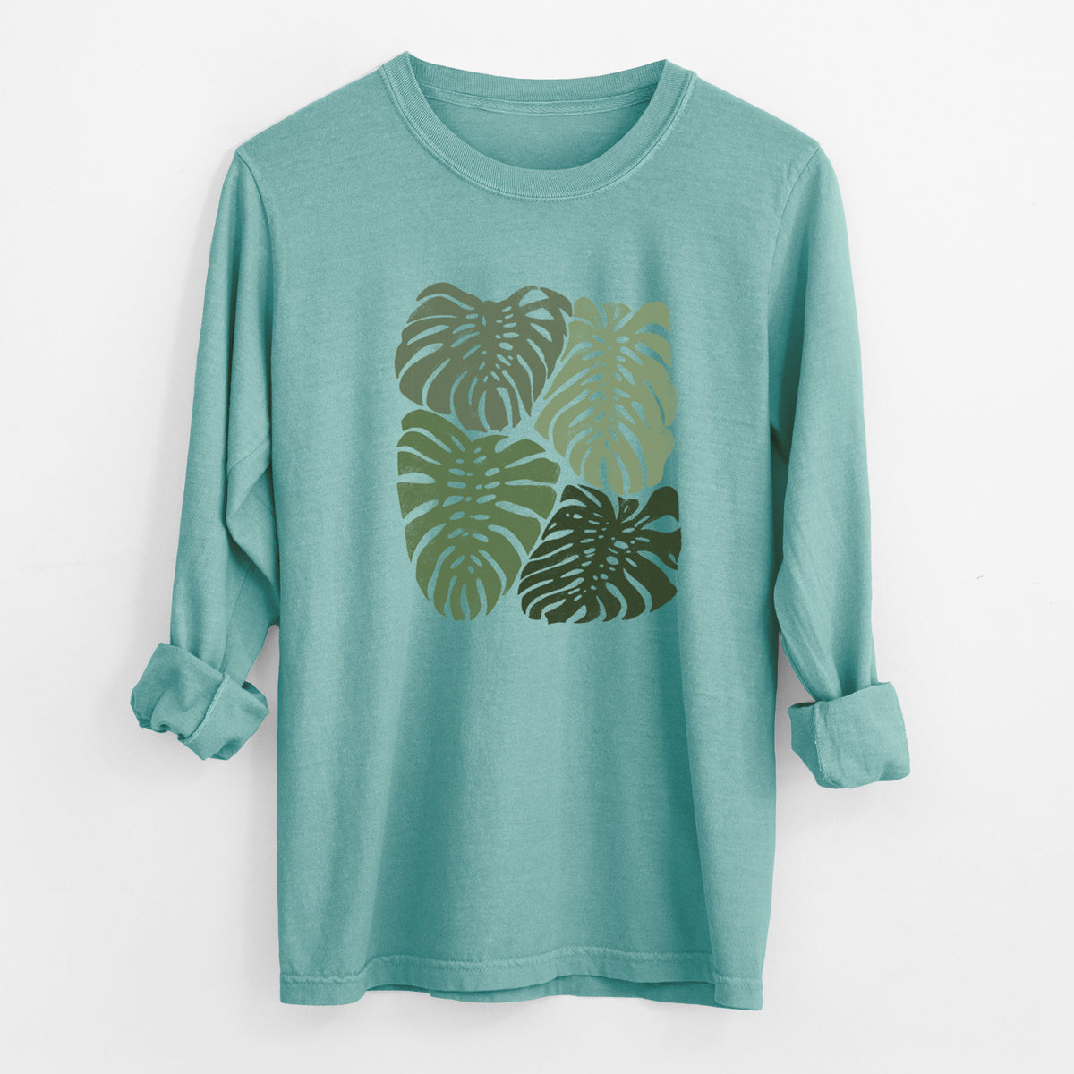 Reef green Comfort Colors long sleeve shirt laid flat with the cuffs rolled, printed with a full-color illustration of large green Monstera leaves filling a square.