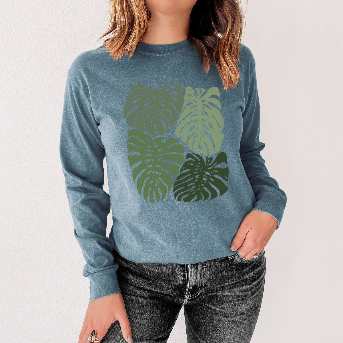 Steel blue Comfort Colors long sleeve shirt printed with a full-color illustration of large green Monstera leaves filling a square, shown in a lifestyle photo.