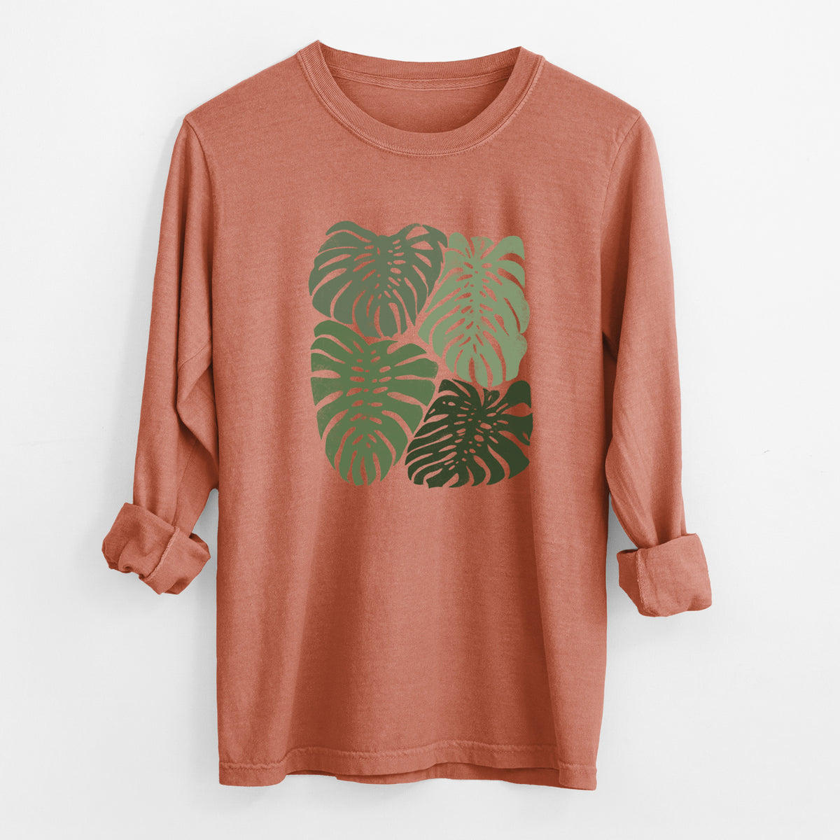 Yam burnt orange Comfort Colors long sleeve shirt laid flat with the cuffs rolled, printed with a full-color illustration of large green Monstera leaves filling a square.