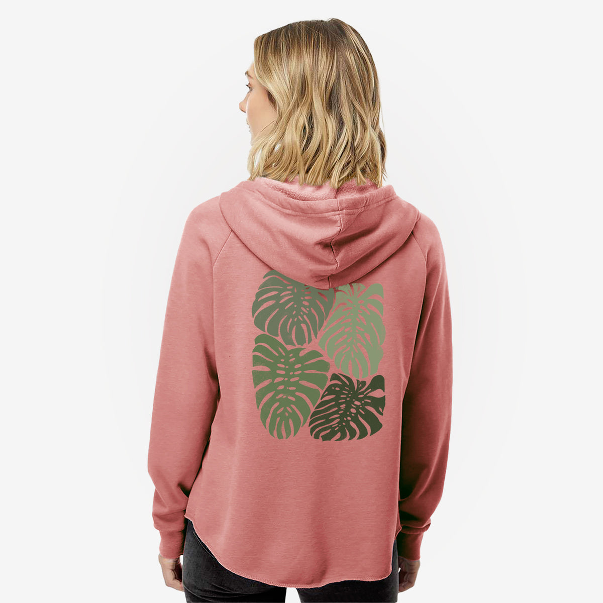 Woman wearing a dusty rose women's Cali Wave zip-up sweatshirt printed with a full-color illustration of large green Monstera leaves filling a square, seen from behind.