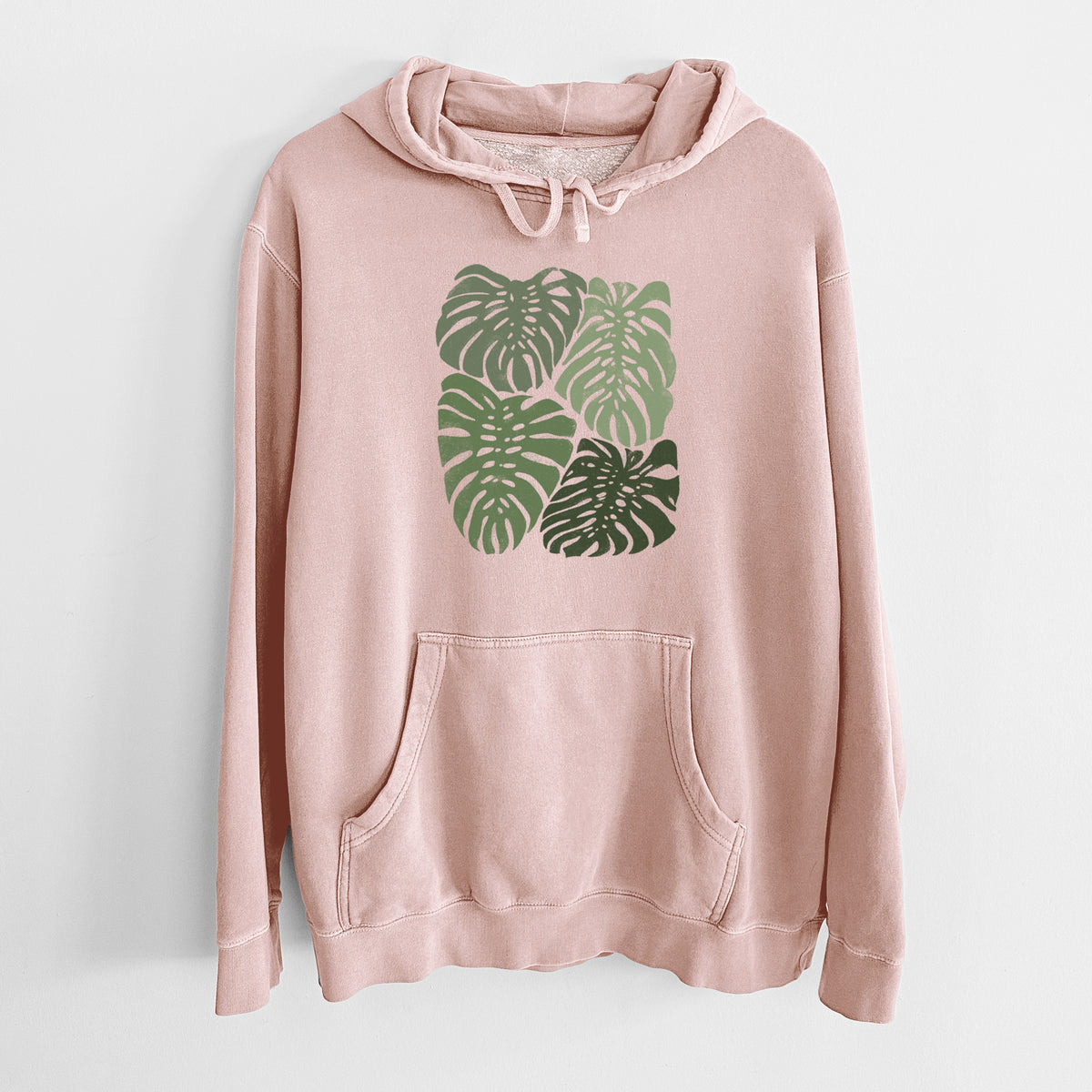 Dusty pink pigment dyed hoodie laid flat, printed with a full-color illustration of large green Monstera leaves filling a square.
