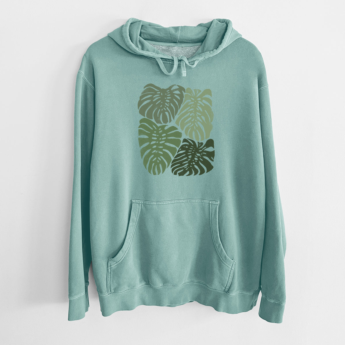 Mint green pigment dyed hoodie laid flat, printed with a full-color illustration of large green Monstera leaves filling a square.