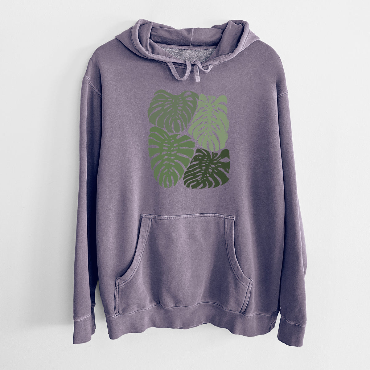 Plum purple pigment dyed hoodie laid flat, printed with a full-color illustration of large green Monstera leaves filling a square.