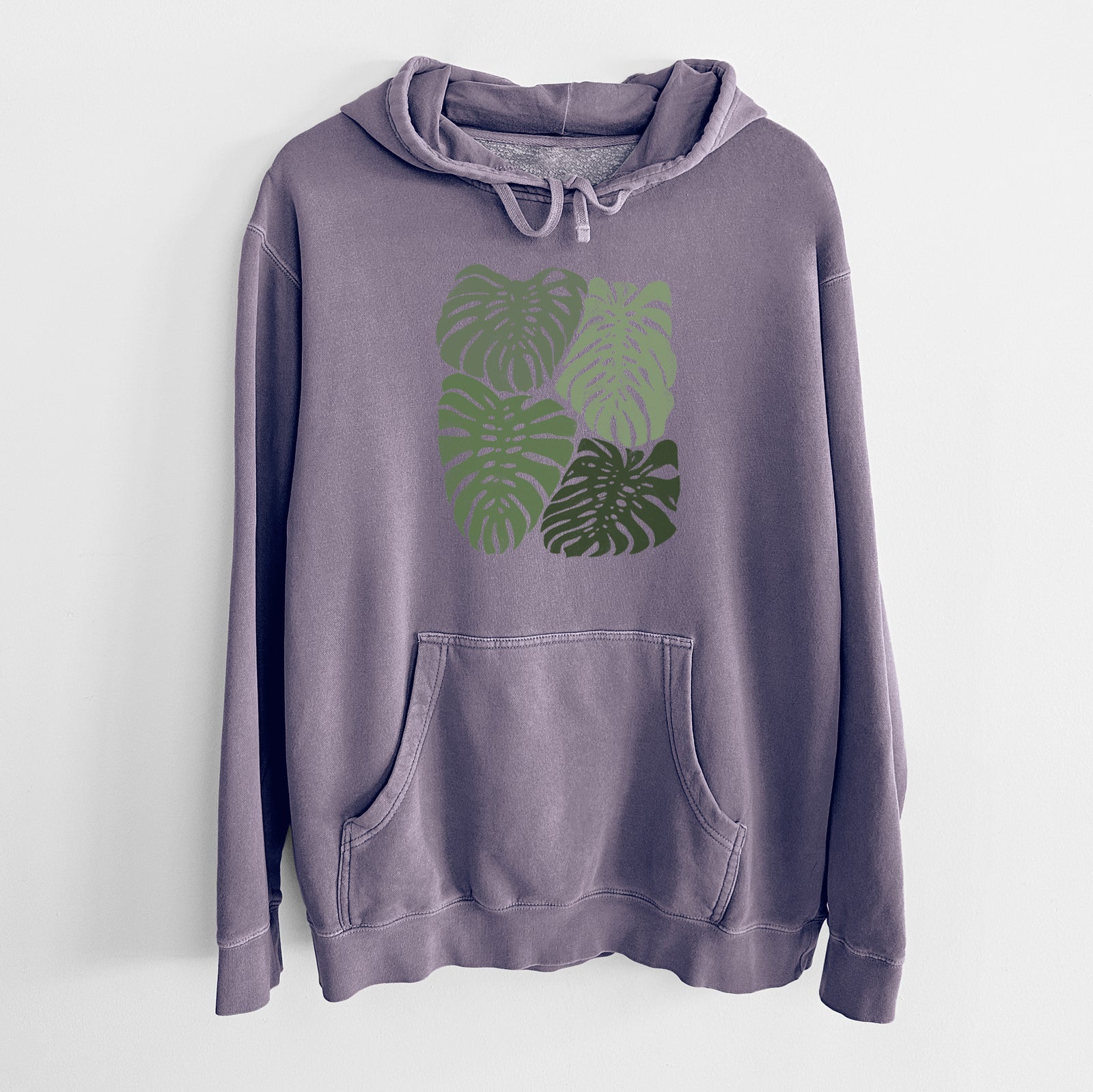 Plum purple pigment dyed hoodie laid flat, printed with a full-color illustration of large green Monstera leaves filling a square.
