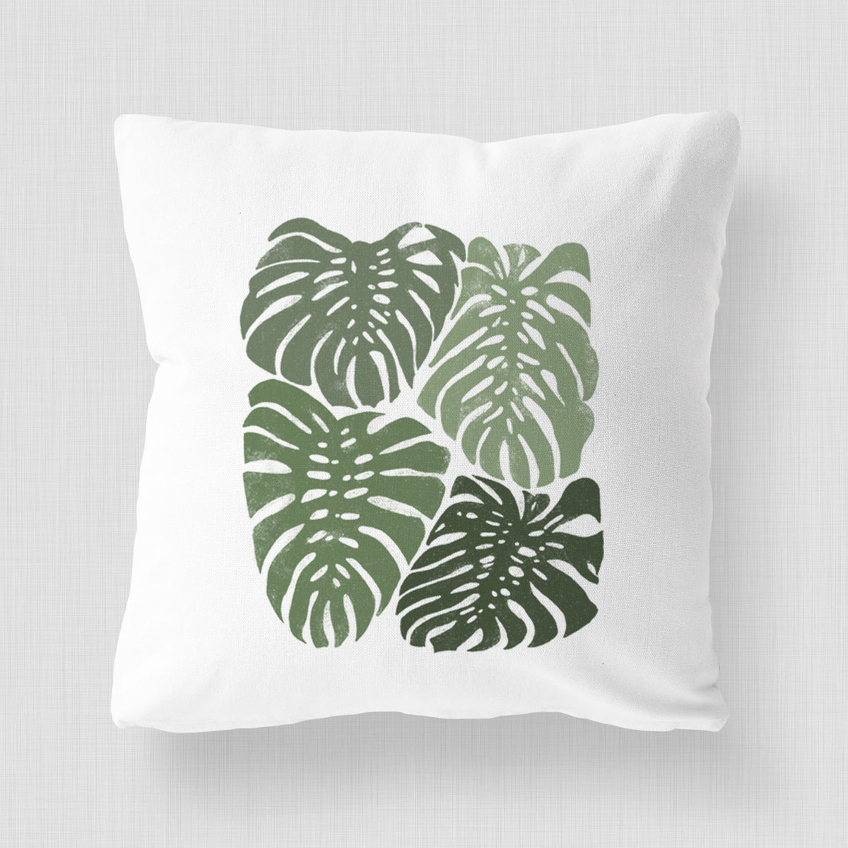 White pillow cover printed with a full-color illustration of large green Monstera leaves filling a square.