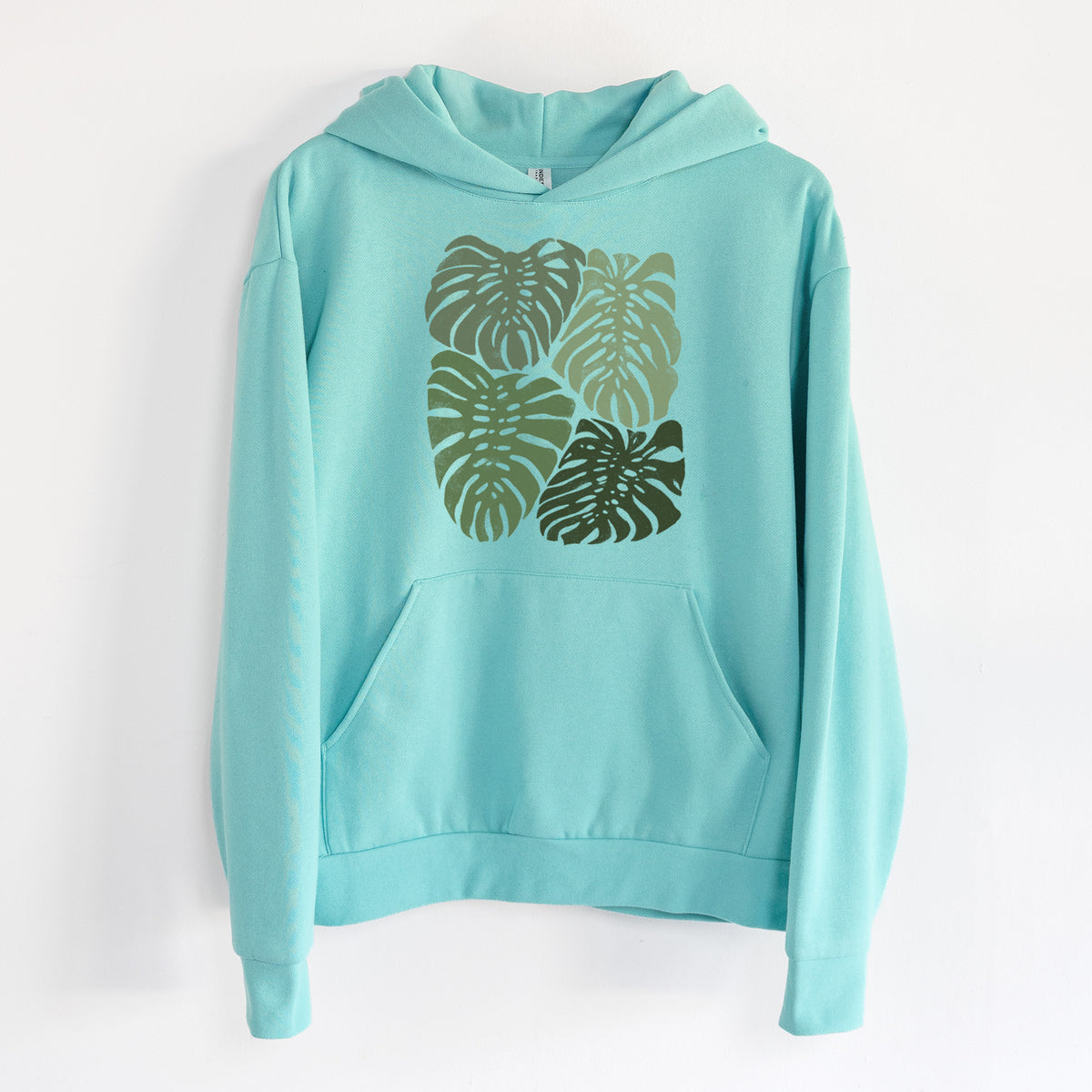 Monstera Vibes - Statement Midweight Hoodie in Seafoam, hanging on a white wall, with a front kangaroo pocket and no drawcords.