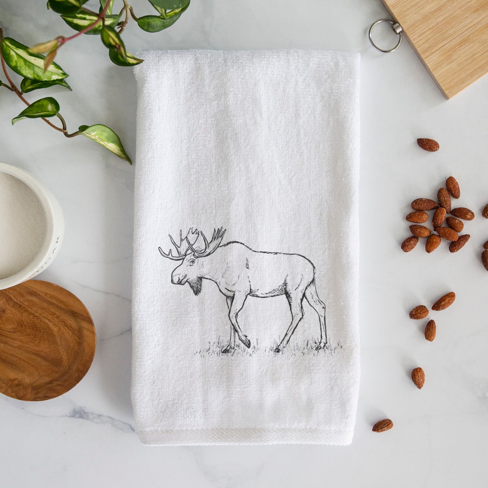 White hand towel printed with a black ink illustration of a bull moose with broad antlers walking.