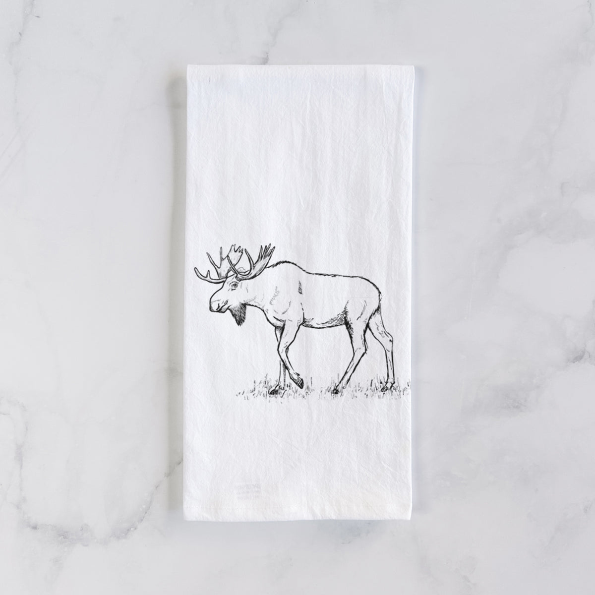 White cotton tea towel laid flat on marble, printed with a black ink illustration of a bull moose with broad antlers walking.