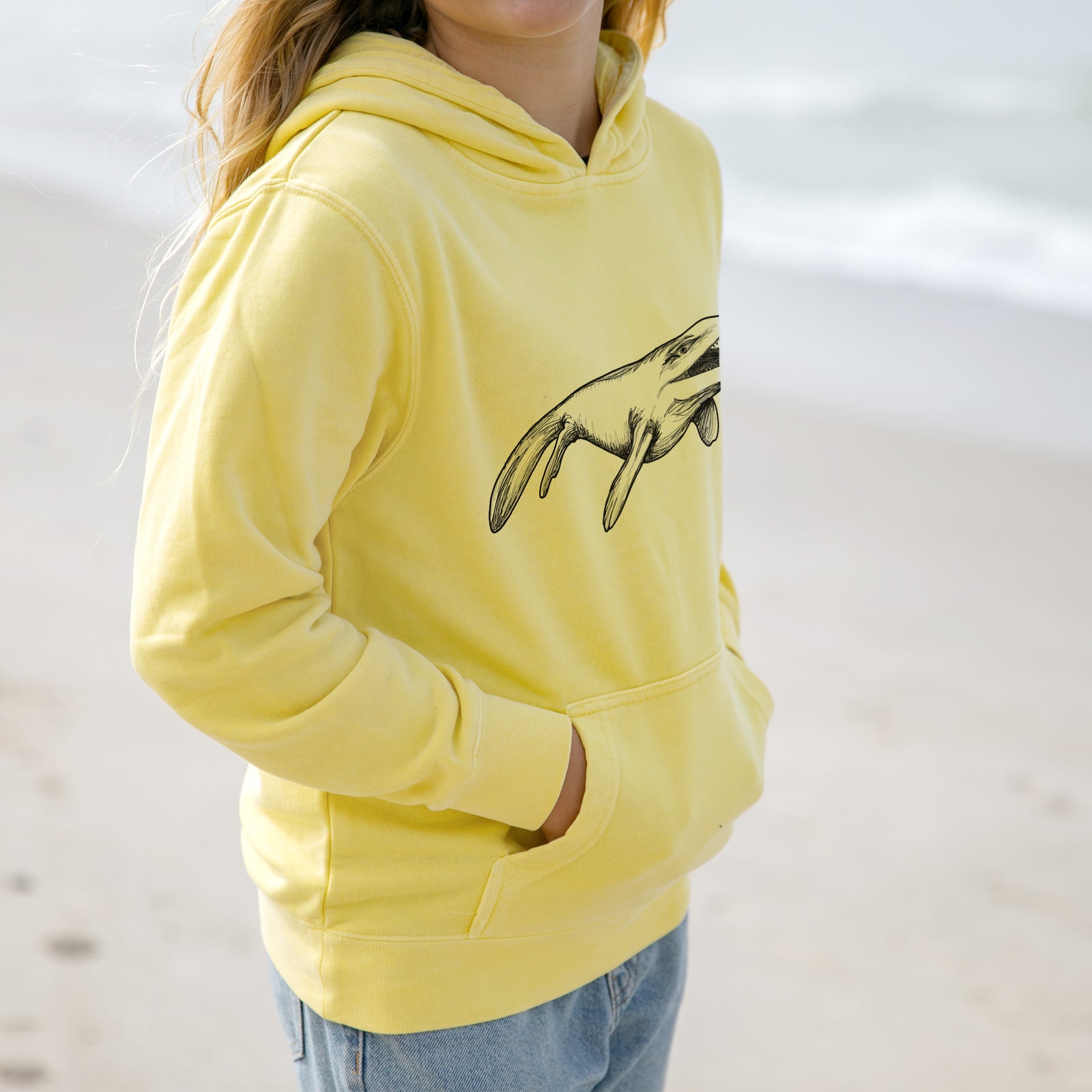 Boy wearing a youth pigment dyed hoodie printed with a black ink illustration of a Mosasaur swimming.
