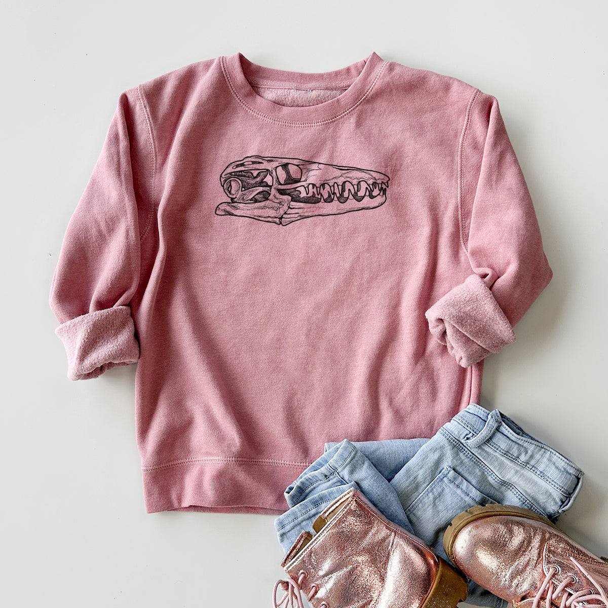 Youth crewneck sweatshirt printed with a detailed black ink illustration of a Mosasaur skull, styled flat with jeans and boots.
