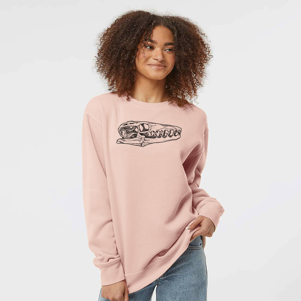 Model wearing a dusty pink pigment dyed crewneck sweatshirt printed with a detailed black ink illustration of a Mosasaur skull.