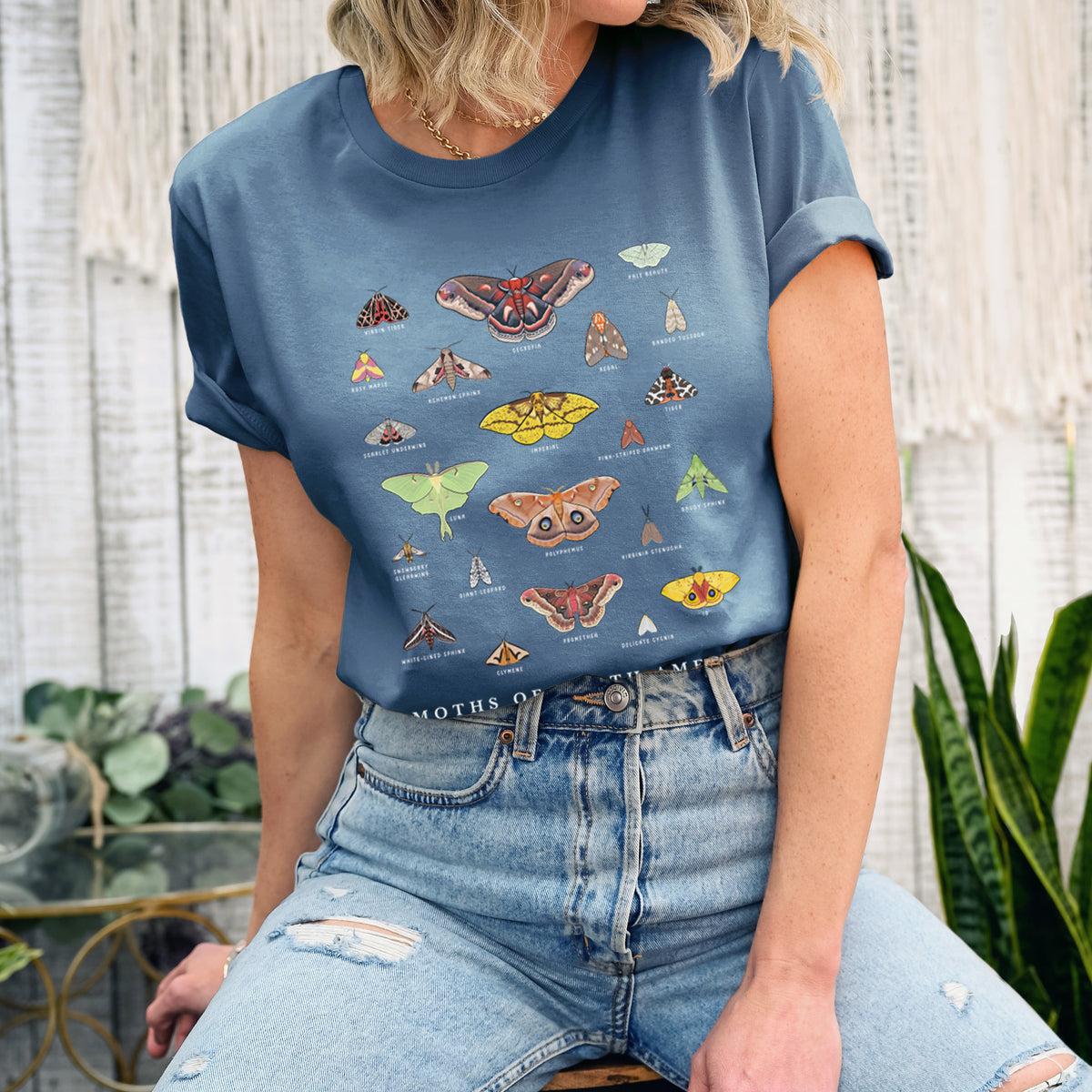 Woman wearing a steel blue lightweight cotton t-shirt printed with a full-color chart of North American moths, each labeled with its species.