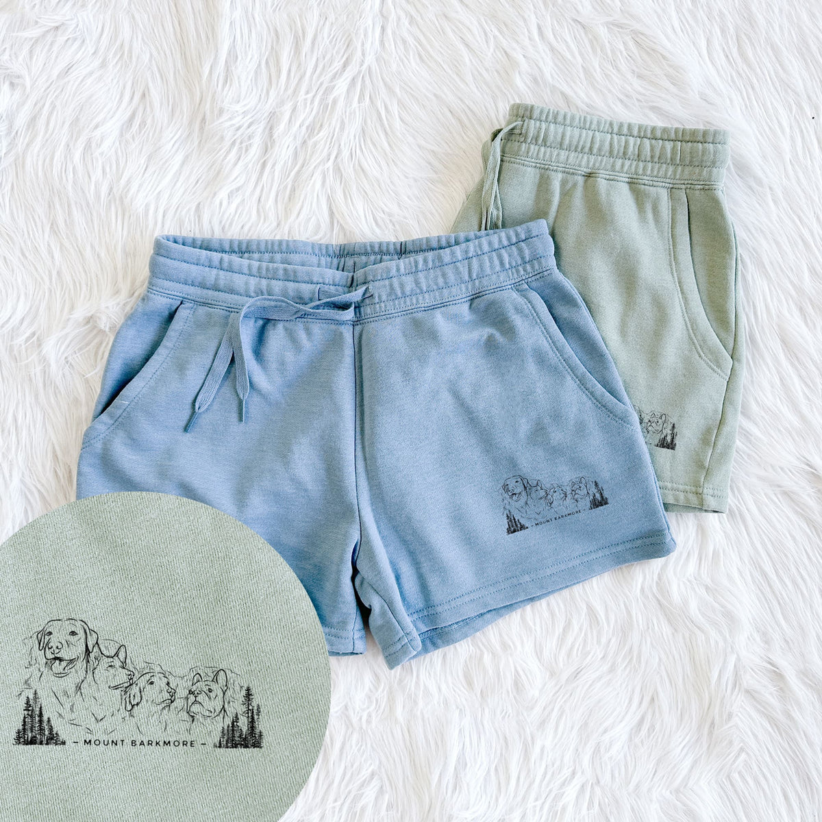 Two pairs of Cali Wave shorts in different colors printed with a black ink illustration of four dog faces carved into a mountain, with the words Mount Barkmore, with a close-up of the print.