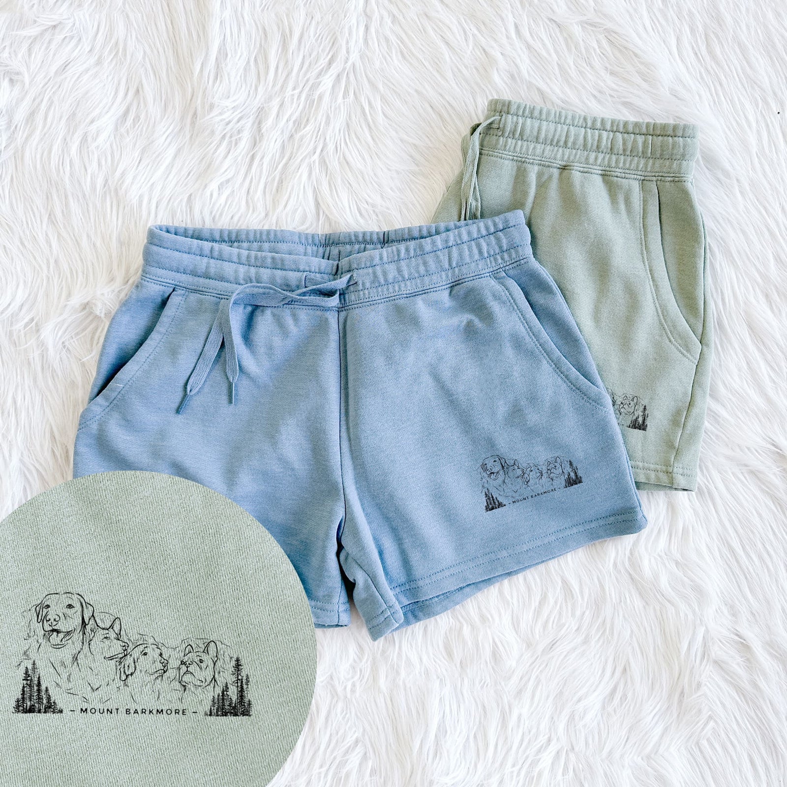 Two pairs of Cali Wave shorts in different colors printed with a black ink illustration of four dog faces carved into a mountain, with the words Mount Barkmore, with a close-up of the print.