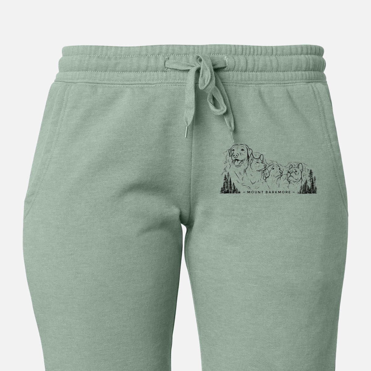 Front of sage green Cali Wave sweatpants, printed with a black ink illustration of four dog faces carved into a mountain, with the words Mount Barkmore on the leg.