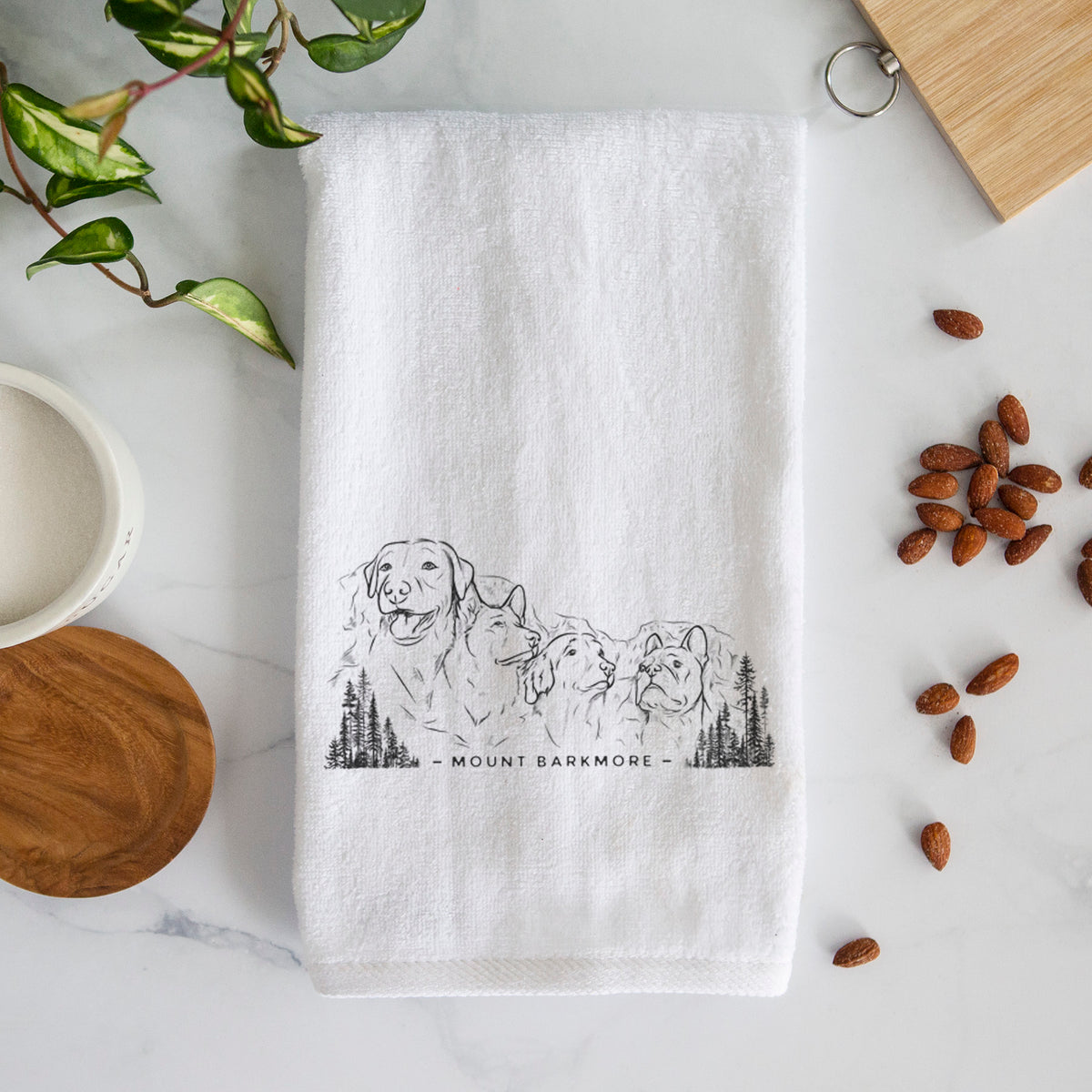 White hand towel printed with a black ink illustration of four dog faces carved into a mountain, with the words Mount Barkmore.