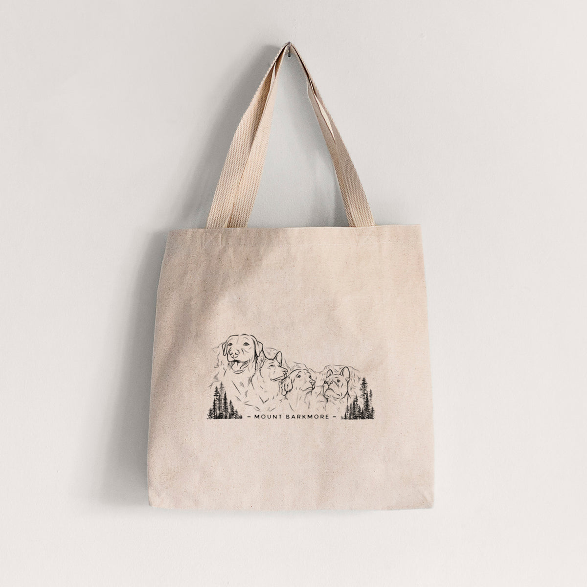 Natural canvas tote bag printed with a black ink illustration of four dog faces carved into a mountain, with the words Mount Barkmore.