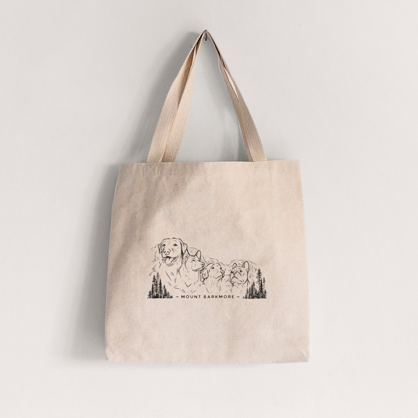 Natural canvas tote bag printed with a black ink illustration of four dog faces carved into a mountain, with the words Mount Barkmore.