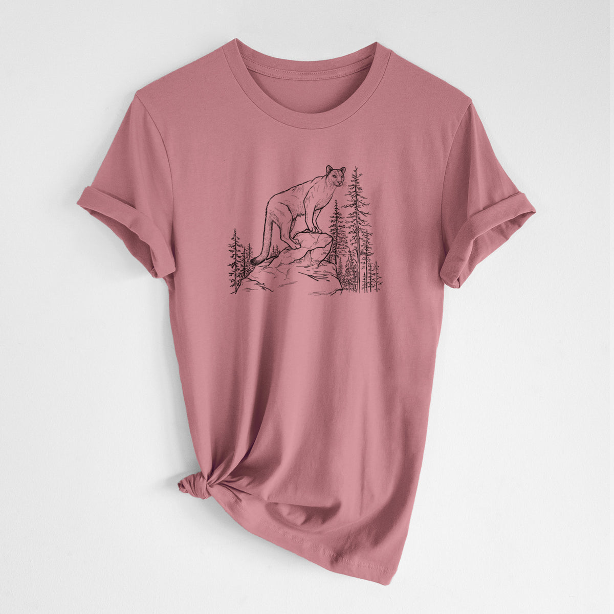Mauve pink lightweight cotton t-shirt laid flat with the sleeves rolled, printed with a black ink illustration of a mountain lion standing on a rocky ledge among pine trees.