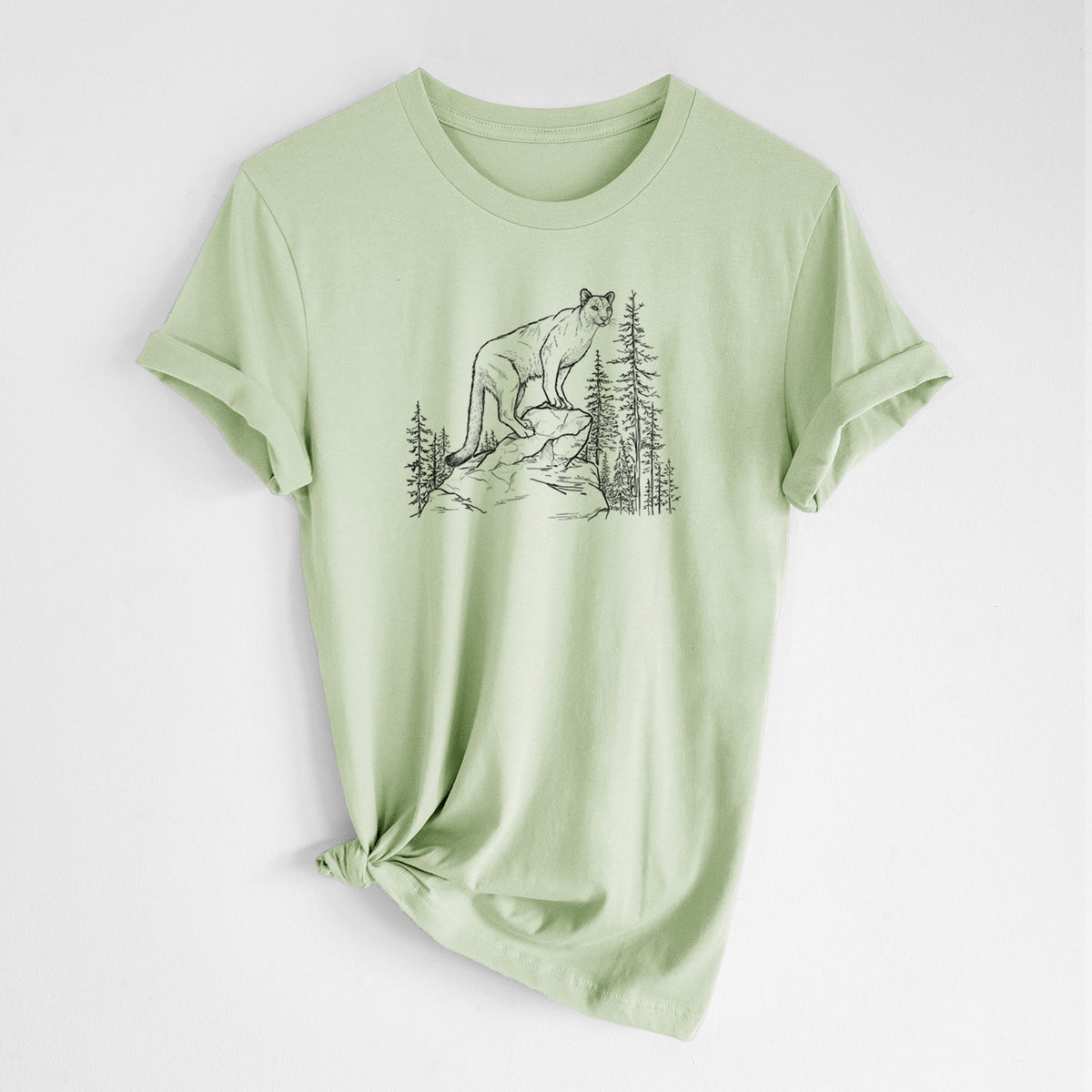 Spring green lightweight cotton t-shirt laid flat with the sleeves rolled, printed with a black ink illustration of a mountain lion standing on a rocky ledge among pine trees.