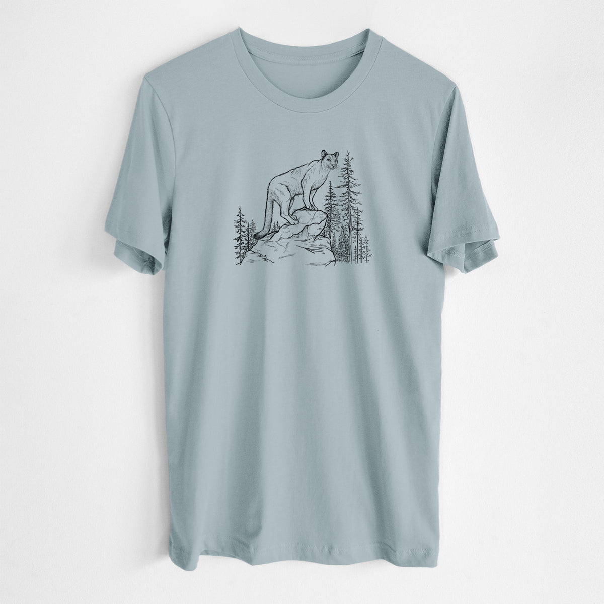 Vintage denim lightweight cotton t-shirt laid flat, printed with a black ink illustration of a mountain lion standing on a rocky ledge among pine trees.