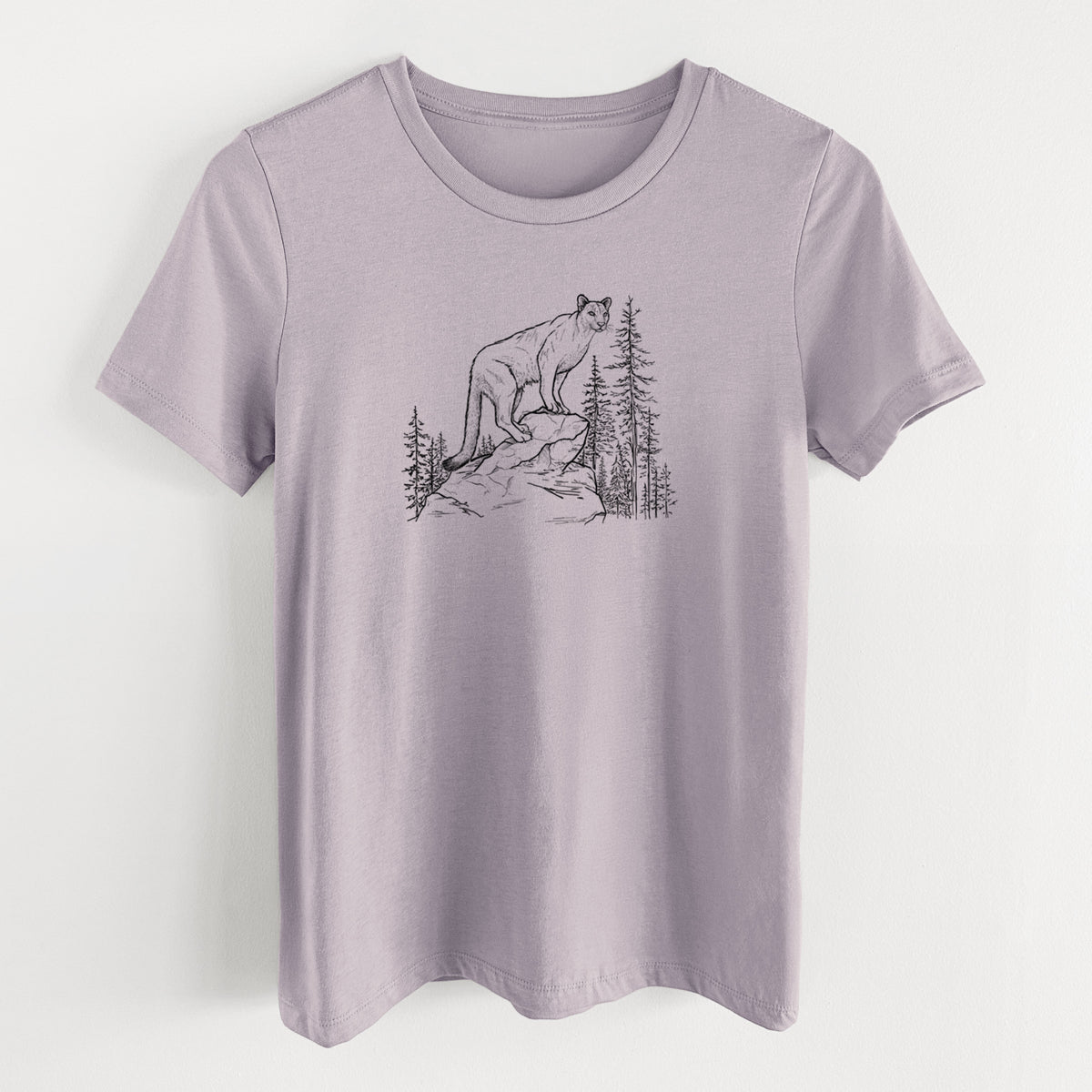 Light violet women's relaxed fit cotton t-shirt laid flat, printed with a black ink illustration of a mountain lion standing on a rocky ledge among pine trees.